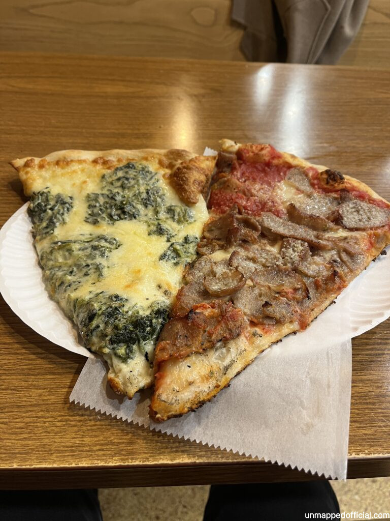 Two slices of pizza on a paper plate on a table. One slice is artichoke cheese and one is sausage. Food diary: What i ate in manhattan nyc. where to eat in new york best places to eat in manhattan