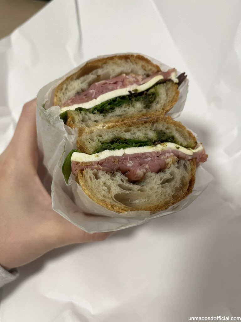 two halves of a sandwich, showing the inside of cheese, greens, and proscuitto
