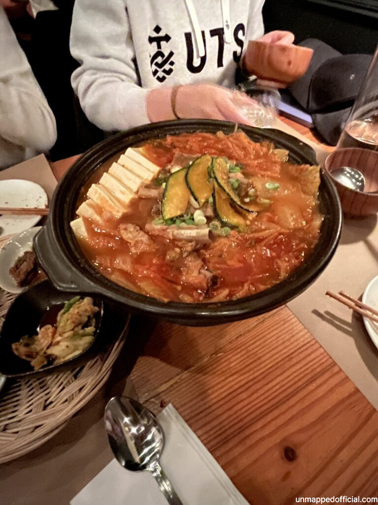 large pot of korean kimchi and tofu stew on a table surrounded by other silverare