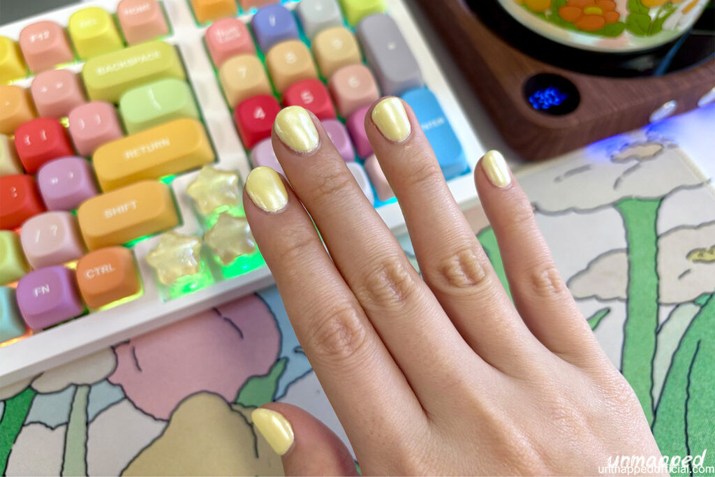 hand posting with trendy butter yellow colored nails and colorful desk background