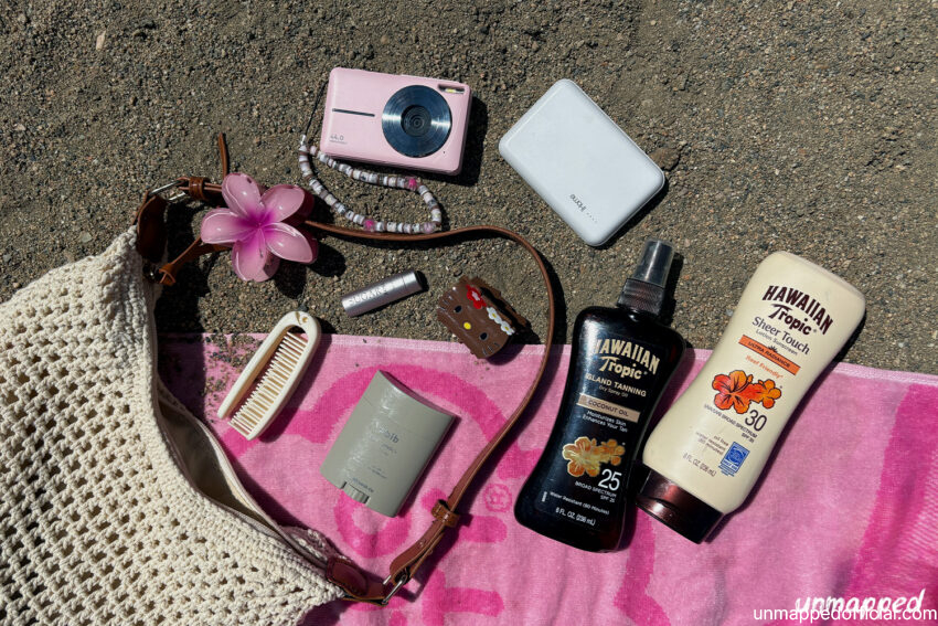 what's in my beach bag? beach bag on towel on sand with bag essential items laid out