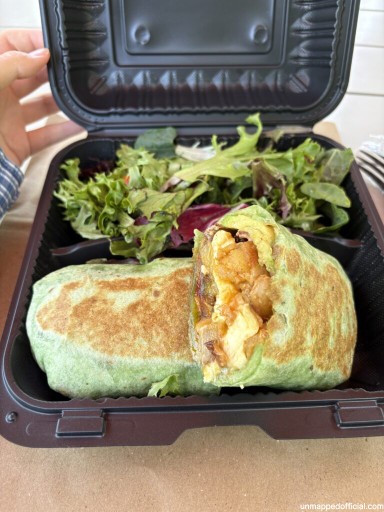 green breakfast burrito with side of salad in a to-go container