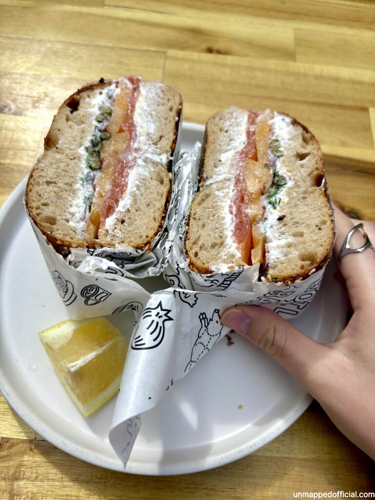 cross section of halved lox bagel on a plate with a lemon wedge