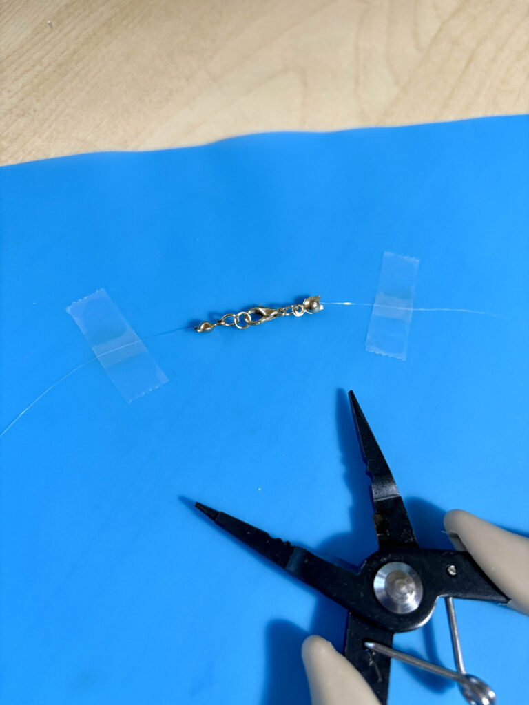 jewelry pliers next to a clasped nylon thread necklace taped down to a silicone mat