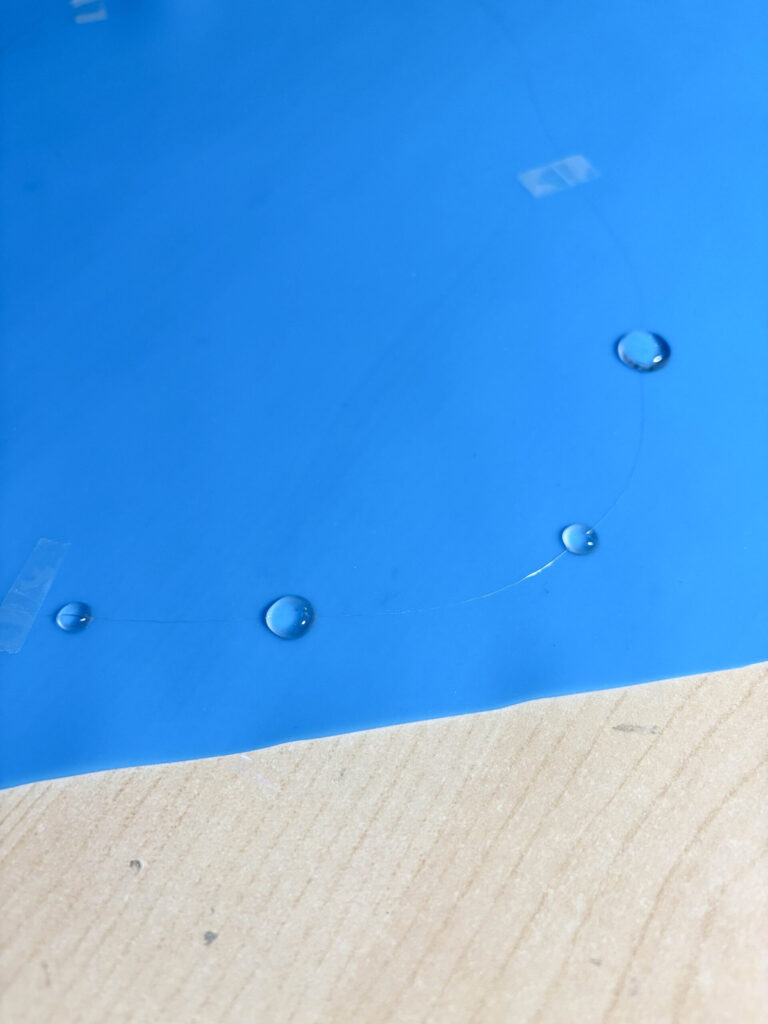 drops of UV resin raindrops on nylon thread necklace that is taped down onto a silicone mat