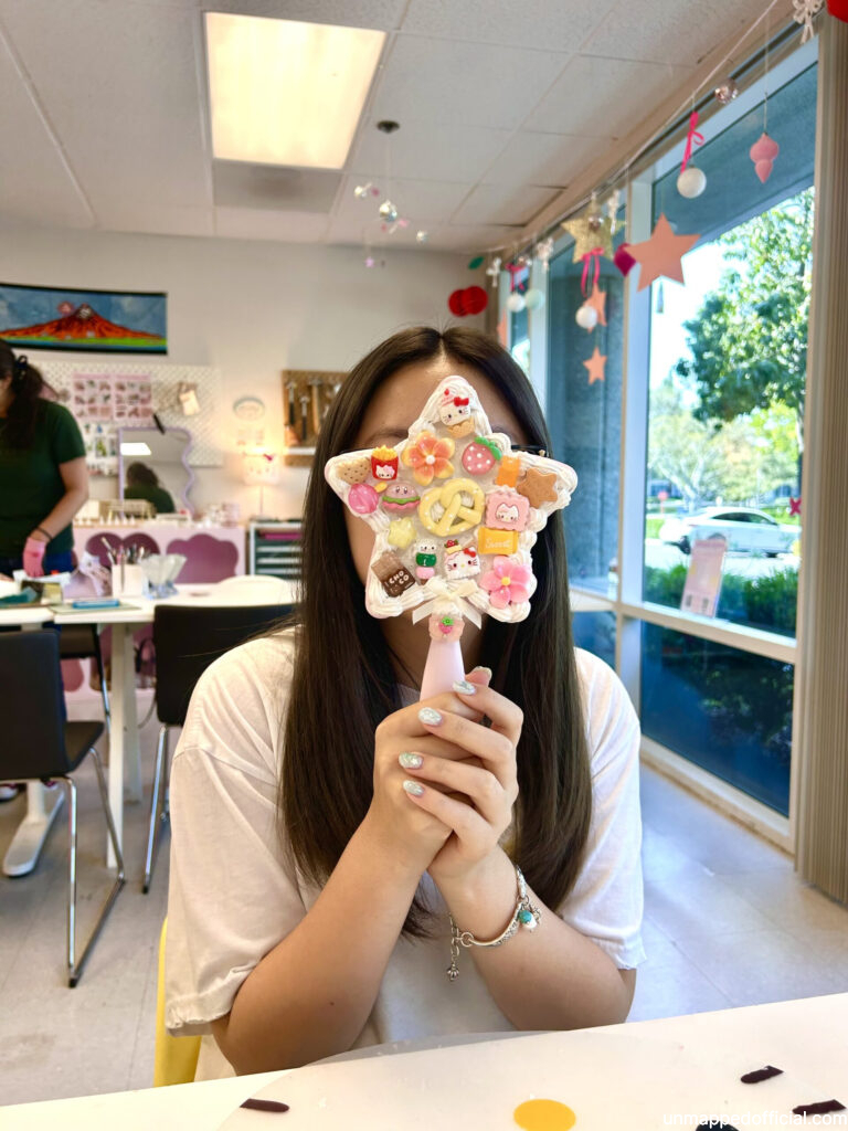 girl holding up decoden mirror in front of her face, displaying her work